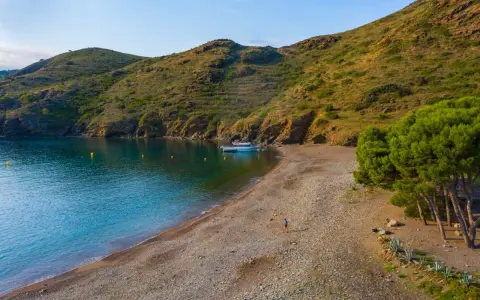 Tranquila cala Joncols plage con aguas turquesas, una persona paseando y barcas amarradas.