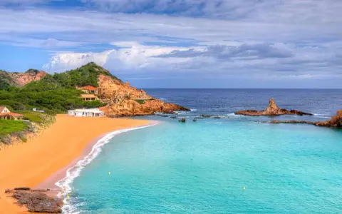 Hermosas calas cerca de Fornells, con arena dorada, aguas turquesas y casas blancas integradas en la costa rocosa.