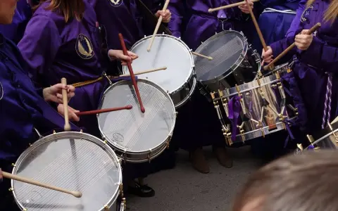 Tambores resonando, parte de las tradiciones de Aragón. Nazarenos con túnicas moradas golpean los parches en una procesión.