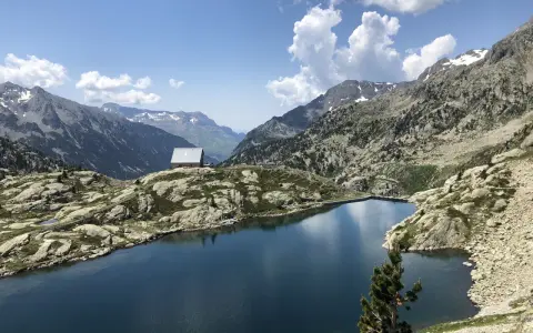 Un refugio solitario junto a los ibones de Bachimaña, rodeado de montañas rocosas y un lago azul intenso bajo un cielo despejado.