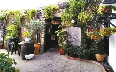 Entrada a un restaurante con vegetación exuberante. Un cartel dice "Restaurante A fuego lento". Ideal para saber donde comer en Hervás.