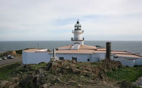 El faro de Cap de Creus se alza blanco y firme sobre rocas escarpadas, vigilando el mar azul.