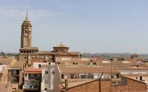 Vista aérea de un pueblo con tejados de teja, destacando una torre de iglesia con reloj. Hay mucho que ver en este pintoresco lugar.