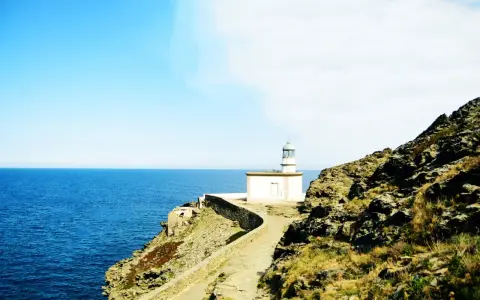 El faro de Cala Nans se alza sobre un acantilado rocoso, vigilando el azul intenso del mar Mediterráneo bajo un cielo despejado.