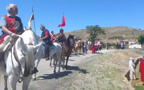 Un desfile ecuestre con trajes históricos, quizás recreando la gesta de el poyo del cid, avanza por un camino rural bajo un cielo azul.
