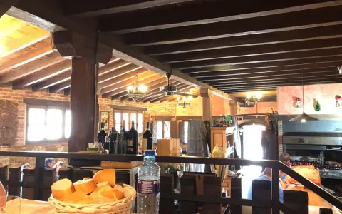 Interior rústico de restaurantes en Llanes, con vigas de madera, ladrillo y una parrilla a la vista. Cesta de pan y botella de agua en primer plano.