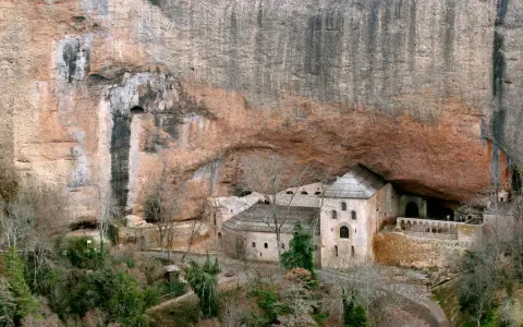 Monasterio de San Juan de la Peña, un impresionante conjunto arquitectónico excavado en la roca, con edificios de piedra y tejados a dos aguas bajo un gran saliente rocoso.