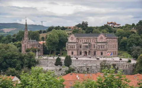 Edificio neogótico y palacio en Comillas, rodeados de vegetación y colinas. Un lugar para ver y disfrutar.