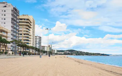 Amplia playa de arena dorada en la playa de Aro centro, con edificios altos a la izquierda y el mar azul a la derecha.