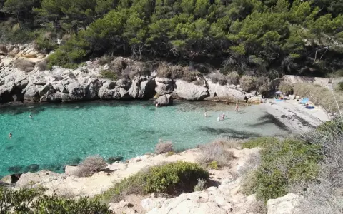 Es caló de la bella dona, una cala escondida con aguas turquesas y rocas escarpadas, donde algunos bañistas disfrutan del sol y el mar.