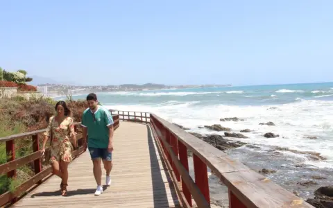 Pareja paseando por un sendero de madera con vistas al mar y la costa de Mijas. ¡Un lugar ideal que ver en Mijas Costa!