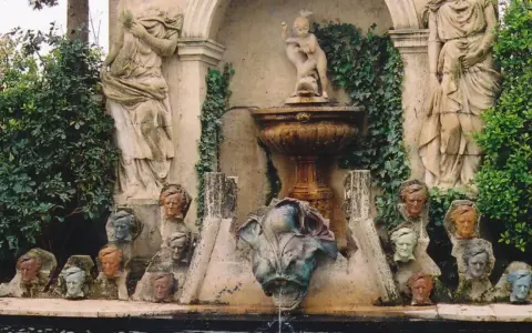 Fuente con estatuas y cabezas de piedra, evocando un antiguo castillo de gala.