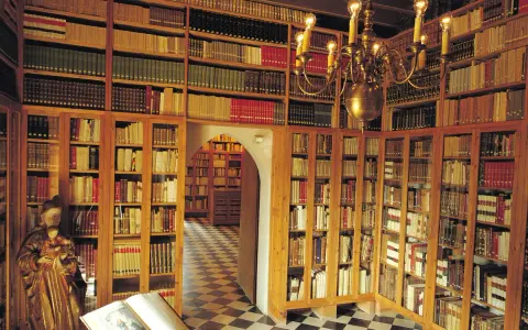 Interior del museu del castell de Peralada, con estanterías repletas de libros antiguos y una lámpara de araña dorada.