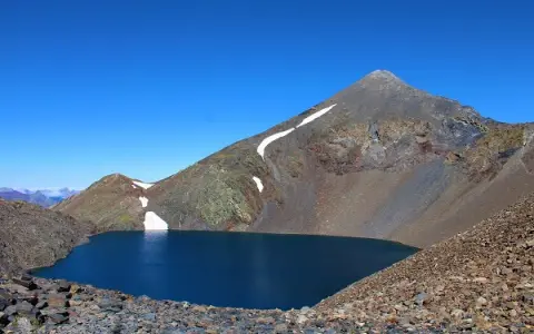 Lago azul profundo en el collado de Tebarray, rodeado de montañas rocosas y con restos de nieve.
