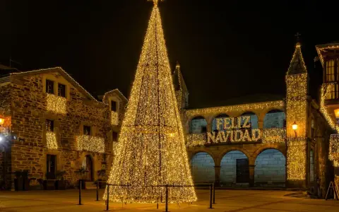 Árbol de Navidad gigante iluminado en una plaza, con edificios adornados y el mensaje "Feliz Navidad". Un lugar ideal que visitar en Navidad en España.