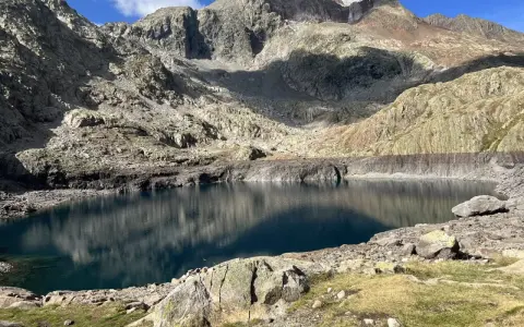 Un lago de montaña de aguas azules profundas, reflejando las cumbres rocosas y el cielo. Un paisaje perfecto para la ruta ibones azules.