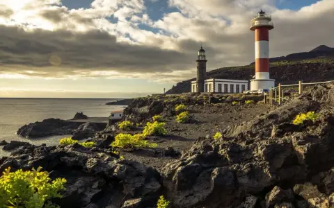 Faros gemelos en la costa rocosa, un destino que ver en La Palma. El mar y el cielo nublado completan la escena.