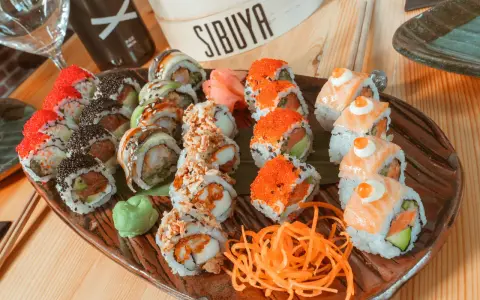 Variedad de sushi en plato marrón, ideal para saber donde comer en Vitoria. Incluye rollos con salmón, huevas de pez volador, aguacate y tempura.