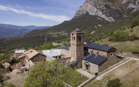 El monasterio de San Victorián, un conjunto de edificios de piedra con tejados oscuros, se alza majestuoso ante una imponente montaña rocosa.