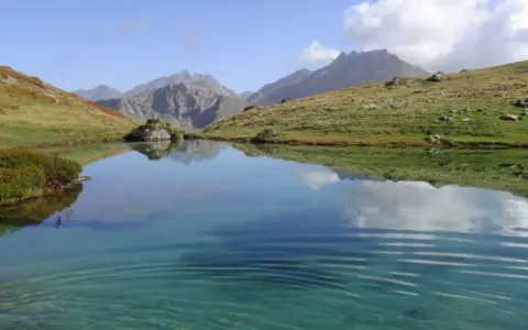 Un sereno ibón de espelunciecha refleja montañas y cielo azul.