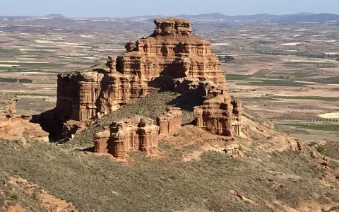 Impresionante formación rocosa en Villarroya de la Sierra, con un paisaje de campos cultivados al fondo.