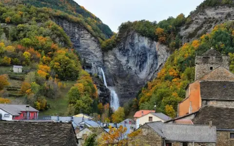 Cascada espectacular en Broto, Huesca, rodeada de bosques otoñales y casas de piedra.