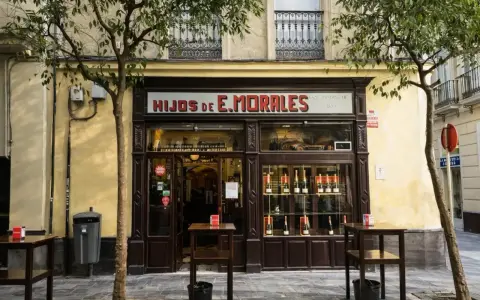Fachada de "Hijos de E. Morales", un bar tradicional en Sevilla, con mesas en la acera y botellas expuestas.