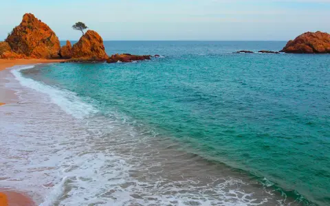 La platja mar menuda, con sus rocas anaranjadas y aguas turquesas, invita a soñar. Una ola rompe suavemente en la arena dorada.
