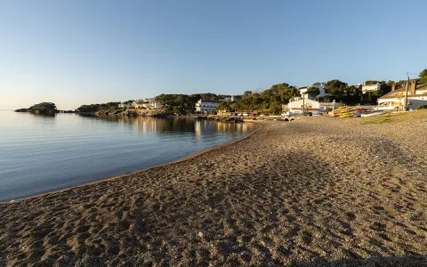 La platja gran de Cadaqués, con casas blancas y kayaks coloridos, se baña en la calma del mar al atardecer.