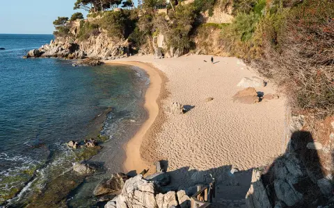 Una persona pasea por la cala belladona, con arena dorada y aguas cristalinas.