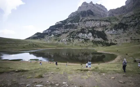 Gente paseando cerca de un lago en el valle de Tena, ideal para rutas de senderismo. Montañas escarpadas al fondo.