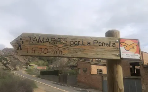 Señal de madera en albelda huesca: "Tamarite por La Penella, 1h 30 min". Al lado, señal de rutas ornitológicas.