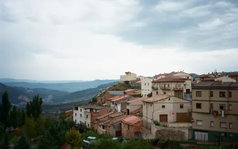 Pueblo español en ladera, con casas de tejados rojos y vistas a montañas. Se ven más de las matas verdes que rodean el asentamiento.