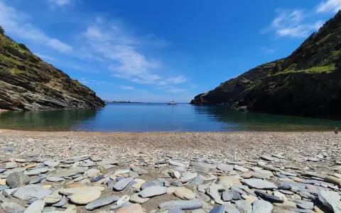 Cala Sa Sabolla, una bahía rocosa con aguas cristalinas y un velero solitario.