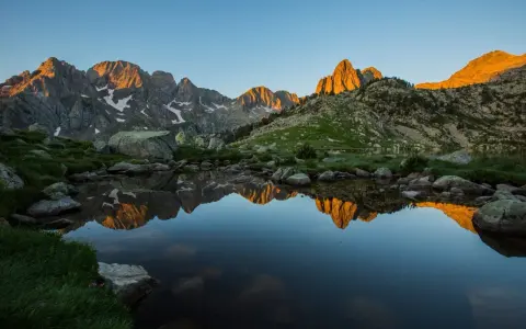 Reflejo dorado de montañas en un lago sereno del **parque natural Posets Maladeta** al amanecer.