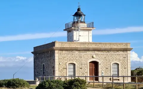 Faro de piedra con torre blanca y cúpula negra, vigilando el mar azul cerca del far port de la selva.