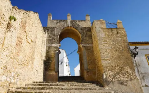 Antigua puerta de Medina Sidonia, con escalinata de piedra y cielo azul. Merece la pena visitar Medina Sidonia.