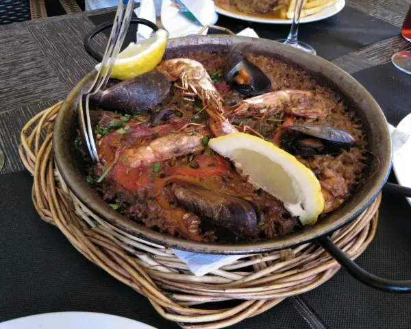 Paella marinera con gambas y mejillones, un plato típico de los restaurantes de Blanes, servida en una paellera sobre una cesta de mimbre.