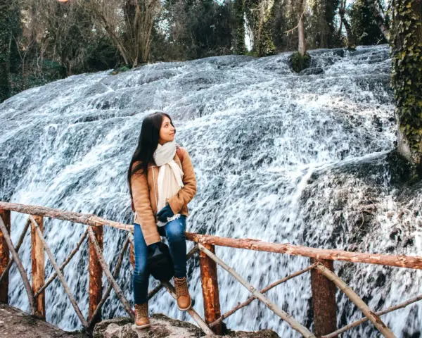 Joven admira la cascada en el Monasterio de Piedra, Zaragoza. El agua cae en cascada sobre rocas cubiertas de musgo, creando un paisaje natural impresionante.