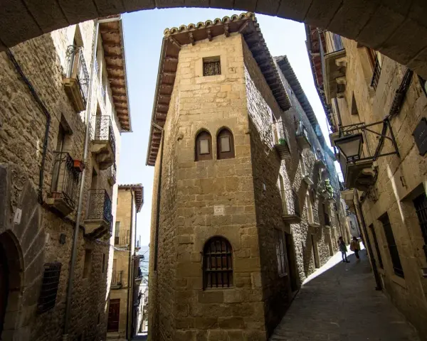 Calle empedrada con edificios de piedra, balcones de hierro y un arco. Un lugar que evoca la historia de los Reyes Católicos.