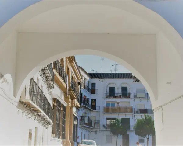 Un arco blanco enmarca edificios blancos y ocres con balcones de hierro forjado. Descubre qué ver en Marchena, un rincón andaluz lleno de encanto.