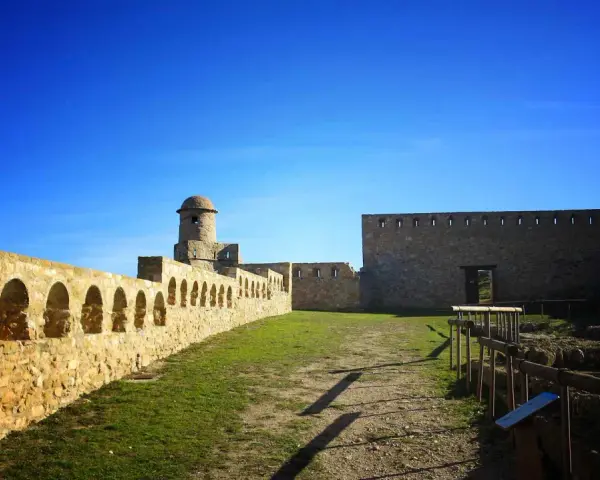 Impresionante castillo de piedra con murallas, arcos y torreón. Un lugar histórico que ver en Benabarre, bajo un cielo azul intenso.