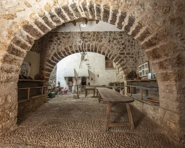 Interior de la torre de las arcas, con arcos de piedra, estanterías rústicas y un horno antiguo.