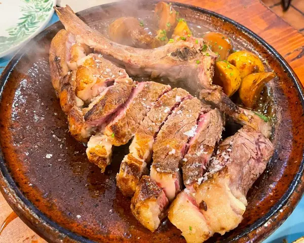 Un jugoso chuletón a la brasa, cortado y servido con patatas asadas, perfecto para comer en Tui.