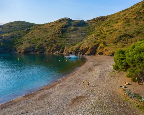 Tranquila cala Joncols plage con aguas turquesas, una persona paseando y barcas amarradas.