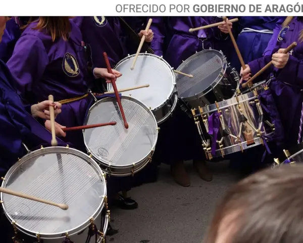 Tambores resonando, parte de las tradiciones de Aragón. Nazarenos con túnicas moradas golpean los parches en una procesión.