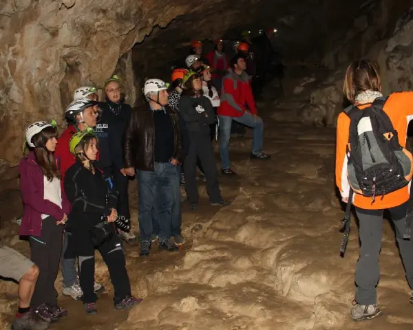 Grupo de exploradores con cascos y linternas en la cueva del oso, observando formaciones rocosas.