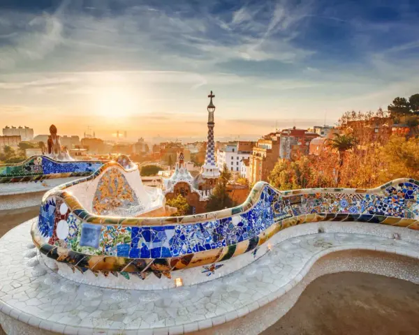 Bancos de mosaico coloridos en el Park Güell, un lugar imprescindible que ver en Barcelona, con la ciudad al amanecer.