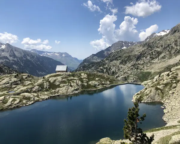 Un refugio solitario junto a los ibones de Bachimaña, rodeado de montañas rocosas y un lago azul intenso bajo un cielo despejado.