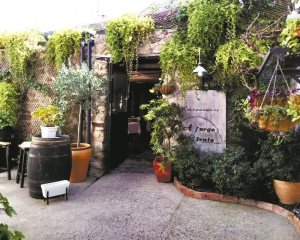 Entrada a un restaurante con vegetación exuberante. Un cartel dice "Restaurante A fuego lento". Ideal para saber donde comer en Hervás.